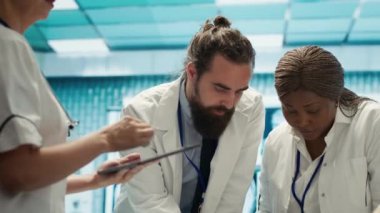 Sağlık ekibi potansiyel tehlikeli teşhisler için test sonuçlarını inceliyor, toplantı sırasında radyografi taramalarına bakıyor. Radyoloji alanında uzman doktorlar hastalık önleme üzerinde çalışıyorlar. Kamera A.