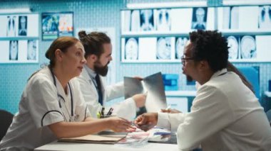 Radyologlar ve uzmanlar röntgenleri incelerler ve özel bir klinikte tıbbi bakımı tartışırlar. Sağlık uzmanlarından oluşan bir ekip, doğru teşhis ve tedavi seçenekleri sunmak için birlikte çalışıyor. Kamera B.