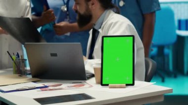 Tıbbi kabinedeki bilgisayarın yanında analitiğe danışan bir grup doktor teşhisi bulmak için röntgen sonuçlarını inceliyor. Lisanslı sağlık görevlileri masasındaki hastane kayıtlarını inceliyor. Kamera A.