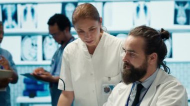 Doktorlar tedavi planlarını geliştirmek için insan anatomisi taramalarını inceleyip potansiyel teşhisi tartışıyorlar. Lisanslı sağlık uzmanları sigorta hizmetleri sağlamak için birlikte çalışıyorlar. Kamera A.