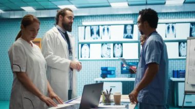 Hastane ekibi röntgenleri inceleyip tedavi stratejisini bir tıp kabinesinde tartışıyor. Radyoloji ve hastalık önleme konusunda uzman doktorlar sağlık hizmetleri için toplu iş yapıyorlar. Kamera B.