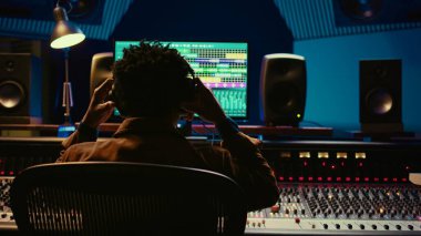 Profesyonel takip mühendisi kayıt odasındaki ses kontrol düğmelerini düzenlemek için kulaklık kullanıyor. Konsol ve yazılımı karıştırma üzerine çalışan bir ses uzmanı. Kamera B.