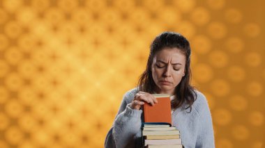 Ders kitaplarını karıştıran, okul sınavı için bilgi toplayan, stüdyo arka planında izole edilmiş bir kadının portresi. Sınav için gerekli kursu kitap yığınları ve kamera A 'da arayan kişi.