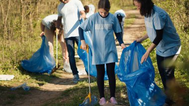 Anne ve kızı ormanı uygun aletler ve çöp torbalarıyla temizliyor. Gezegeni kurtarmak için çöpleri toplayıp geri dönüştürüyorlar. Eylemciler orman kirliliğini durdurmak için çöp topluyor. Kamera A.
