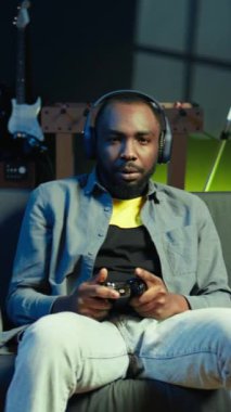 Dikey video, kulaklık takan neşeli adam, video oyunundaki zaferden sonra kutlama, neon ışıklı daire. Kanepede oturan kişi, konsoldaki maçı kazandıktan sonra heyecandan havaya yumruklar savurur.