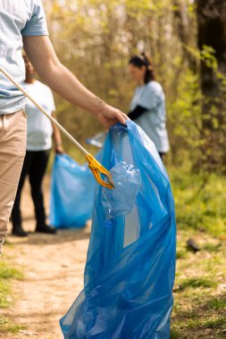 Eylemci, çöpleri çöpte depolamak ve doğal çevreyi temizlemek için ormandan çöp ve plastik atık toplamak için maşa kullanıyor. Erkek gönüllü çöp ve çöp topluyor..