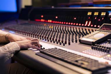 Ses mühendisi, kontrol odasındaki panel panelindeki amfi düğmelerini ve şalterleri çeviriyor. Müziği düzenlemek ve ustalaştırmak için karıştırma konsolu kullanıyor. Müzik stüdyosunda profesyonel yapımcı..