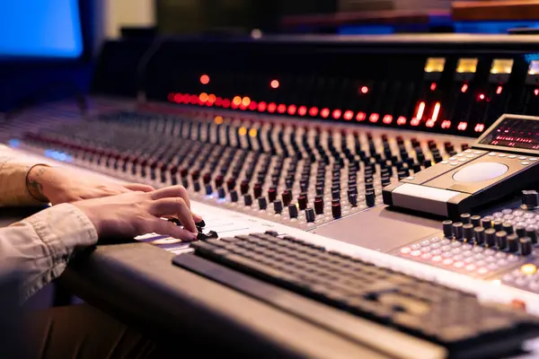 stock image Audio engineer twisting pre amp knobs and switchers on panel board in control room, using mixing console for editing and mastering music. Professional skilled producer in music studio.