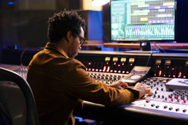 Afrikalı Amerikalı müzik bestecisi bir albüm için yeni bir müzik yaratıyor, kontrol odasında konsolda melodileri düzenliyor ve karıştırıyor. Bilgisayar üzerinde dijital yazılım kullanan ses teknisyeni, ses ayarlarını ayarla.