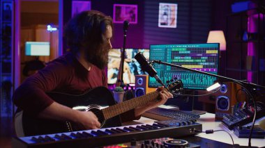 Müzik yapımcısı şarkı söylüyor ve akustik gitar çalıyor. Yeni bir melodi kaydetmek için kişisel stüdyosunda çalışıyor. Ses mühendisi kayıt melodileri, konsol ses paneliyle düzenleme. Kamera B.