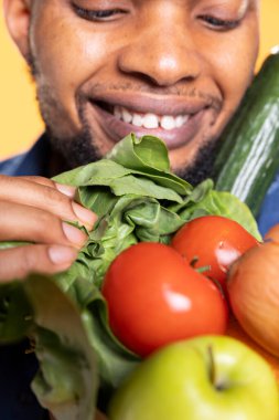 Afrika kökenli Amerikalı bir adam, stüdyodaki taze meyve ve sebzelerin kokusunu koklayarak, bir kese kağıdındaki olgun ürünlere bakar. Biyolojik organik malzemelerle aşçı. Kapat..