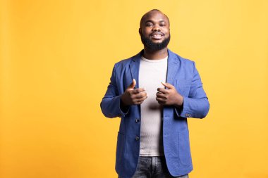 Kendine güveni olan havalı ve aklı başında bir Afrikalı Amerikalının portresi, sarı stüdyo arka planında izole edilmiş. Etkileyici BIPOC çalışanı şık görünüyor, umursamazca poz veriyor.