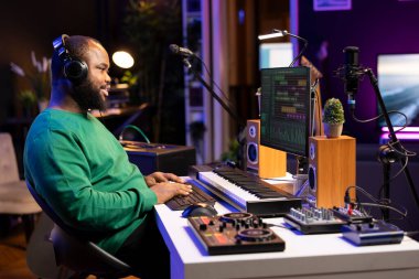 Afrika kökenli Amerikalı yapımcı ses ve melodileri karıştırarak kulaklıktaki son ürünü dinliyor. Ses teknisyeni DAW yazılım arayüzü ve stereo ekipmanı ile bilgisayar üzerinde çalışıyor.