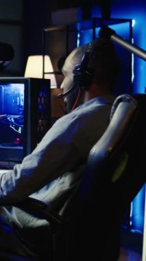 Dikey video oynatıcı klavye, fare ve kulaklık kullanarak PC 'de birinci şahıs nişancı video oyunu oynuyor, boş zamanların tadını çıkarıyor. Oturma odasındaki adam düşmanları yok etmek için yüksek teknoloji bilgisayar periferlerini kullanıyor.