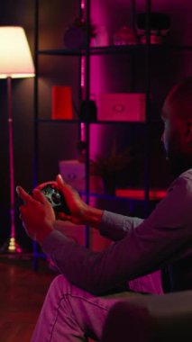 Dikey video oynatıcı, büyük akıllı TV 'de birinci şahıs nişancı oyunu oynamak için kontrol ve kulaklık kullanıyor. Ev sinemasındaki adam düşmanları yenmek için yüksek teknoloji oyun konsolunu kullanıyor, kamera B