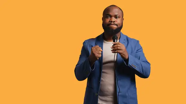 stock image Aggressive lecturer holding motivational speech using microphone, gesturing with hands, isolated over studio background. Speaker urging spectators to take action, doing speech using mic