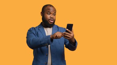 Gülümseyen Afro-Amerikalı adam, telekonferans toplantısında arkadaşlarını selamlıyor. Akıllı telefon, stüdyo geçmişi kullanarak. Dost canlısı el sallayan kişi, internette selam veren arkadaş, kamera A