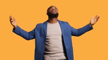 Neşeli, dindar, Afro-Amerikan bir adam gökyüzüne bakıp Tanrı 'sından işaret bekliyor. Mutlu ruhani adam el hareketi yapıyor, mucize bekliyor, stüdyo arka planında izole edilmiş, kamera B