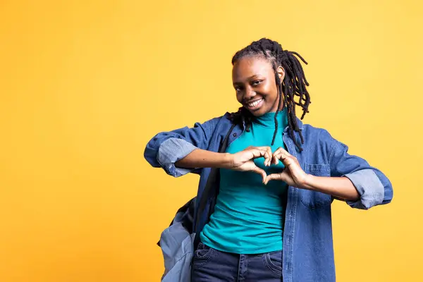 stock image Portrait of loving joyous african american woman doing heart symbol shape with hands. Happy caring BIPOC person showing love gesturing, isolated over yellow studio background