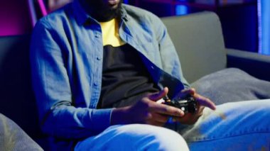 Kanepede oturan oyuncu evde video oyunu oynamak için kulaklık ve kumanda kullanıyor. Kapat. Ev sinemasındaki adam yüksek teknoloji oyun konsolu oyun sahasını kullanarak rakiplerini yeniyor, kamera A