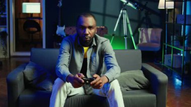 RGB 'deki oyuncu ev oyunlarını joystickle aydınlatıyor ve rahatlama zamanının tadını çıkarıyor. Neon ışıklı oturma odasında kanepede oturan adam kumanda, kamera B kullanarak konsolda video oyunları oynuyor.