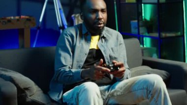 Kanepedeki oyuncu Esports video oyunu turnuvasını kazanmasını kutluyor, arkadaşlarıyla internetten oynuyor. Oyuncu, şampiyonluk maçından sonra seviniyor. Takım arkadaşlarıyla çok oyunculu maçın keyfini çıkarıyor. Kamera A.