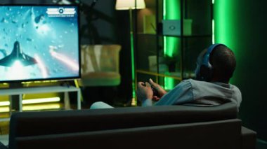 Uzay gemisi uçan video oyunu oynayan adam büyük akıllı TV 'de, kulaklık takıyor. Oyuncu oyun konsolunda SF atari oyunundan zevk alıyor, Gamepad, kamera A kullanarak galakside uzay aracına pilotluk yapıyor