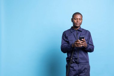 Silahlı güvenlik görevlisi cep telefonundaki mesajlara cevap veriyor, mavi arka plandaki işine ara veriyor. Genç yetenekli koruma sosyal medya uygulamalarını kontrol ediyor, akıllı telefonları tarıyor..