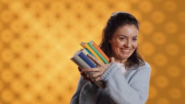 Excited woman delighted about books ordered, treasuring them, isolated over studio background. Euphoric reading enthusiast cherishing stack of novels, feeling lively and overjoyed, camera A clipart