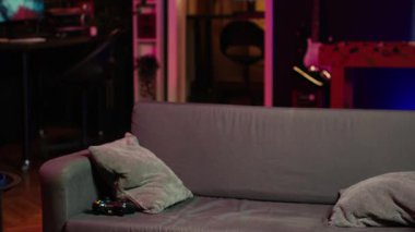 Adam eve geliyor, oyun oynuyor ve eğleniyor. Neon ışıklı oturma odasında koltukta oturan adam, konsolda video oyunu oynuyor, yoğun bir iş gününden sonra dinleniyor, kamera A