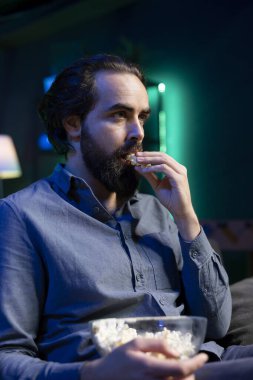 Televizyonda kablolu yayını izlerken patlamış mısırın tadını çıkaran adam sahnelerden büyülenmiş. Oturma odasındaki koltukta büyülenmiş seyirci abur cubur yiyor ve sürükleyici televizyon dizilerine bakıyor.