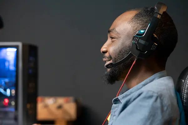 stock image Joyful man having fun playing videogames on desktop computer, chatting with teammates through headphones mic. Relaxed gamer communicating with friends through headset microphone during game at home