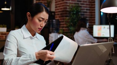 İş kadını, önemli bir iş toplantısına hazırlanmak için dizüstü bilgisayarla evrak arasında veri taraması yapıyor. Finansal istatistikleri online şirket bilgileriyle karşılaştıran işçiler