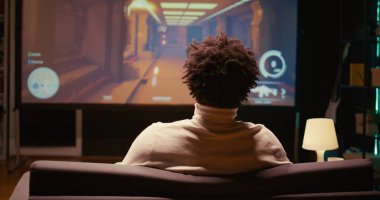 BIPOC man playing shooter videogame on ultrawide smart TV in futuristic industrial setting with health, stamina, ammo bars HUD overlay. Zoom in shot of gamer enjoying PvP fps online multiplayer game clipart