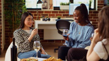 Asyalı kadın aperatifleri yerken çok ırklı apartman misafirleriyle sohbet ediyor. Ev sahibi arkadaşlarıyla iletişim kurarken şarküteri tabağından gurme peynirin tadını çıkarıyor.