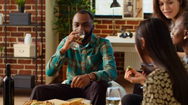 Neşeli Afrikalı Amerikalı adam BIPOC 'un parti davetlileri arasında ilginç bir sohbete yardım ediyor. Oturma odasında çeşitli arkadaş gruplarının anlattığı ilginç hikayeleri dinlemekten mutluluk duyarız.