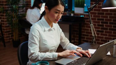 Gülümseyen Asyalı çalışan, bilgisayar masasında bir fincan kahvenin yanına önemli e-postalar yazıyor. Bilgisayarda yazan neşeli bir çalışan, görevleri çözen, iş ortaklarıyla iletişim kuran.