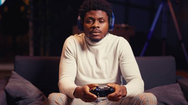 BIPOC 'un portresi kulaklık takan ve yoğun online video oyunu oynayan, kontrol düğmelerine spam atan bir adam. İnternet ihracat yarışmasına katılan oyuncu, oyun konsolunda oynuyor, kapatın