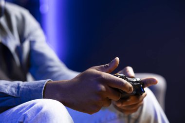 RGB 'deki oyuncu ev oyunlarını oyun alanıyla aydınlatıyor, eğleniyor. Neon ışıklı oturma odasındaki koltukta oturan adamı yakın plan çekimde kumanda kullanarak konsolda video oyunları oynarken çek.