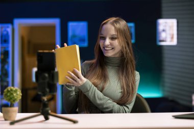 Neşeli Z içerik yaratıcısı, okuyuculara özet sunarak akıllı telefonu tripodun üzerinde kullanarak kitabın video incelemesini kaydeder. Medya yıldızı, abonelere yeni çıkan ve telefonla kaydedilen romanı gösteriyor