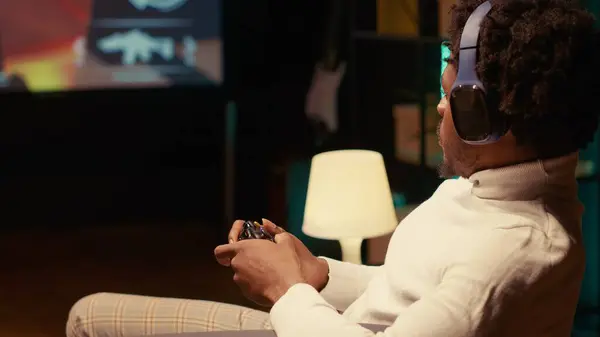 stock image Gamer playing first person shooter game on ultrawide smart TV, communicating with teammates using headphones. African american man reaching final mission in FPS videogame