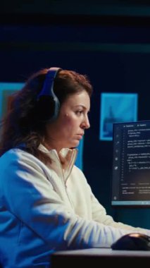 Yazılım kalitesi güvencesi verirken müzik dinleyen dikey video kadını, bilgisayar ekranında kaynak kodları okuyor. Kulaklık takan geliştirici, podcastların keyfini çıkarıyor ve masaüstü bilgisayarındaki kodlamayı denetliyor
