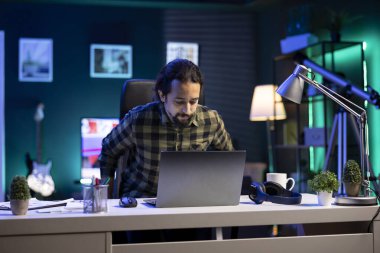 İçeride çalışan, teknoloji meraklısı bir adam masaya oturur ve birden fazla iş yapabilme becerisini kolayca gösterir. Sakallı adam bilgisayarını araştırma ve e-posta kontrolü için kullanmaya hazırlanıyor..