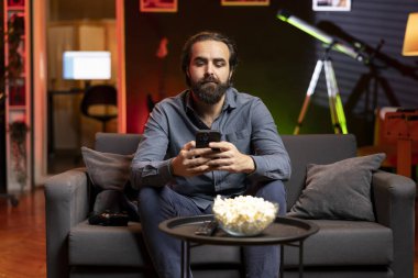 Video oyununa ara veren bir adam elinde akıllı telefonla neon ışıklı odada arkadaşlarına mesaj atıyor. Oturma odasındaki oyuncu cep telefonuyla arkadaşlarıyla konuşmak için oyunu durduruyor