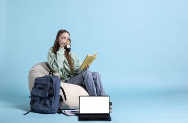 Kahve içen ve ders kitabı okuyan öğrenci portresi, üniversite sınavlarına hazırlanmak, stüdyo geçmişi. Zor ev ödevleriyle başa çıkmak için kafeinli içecek tüketen bir genç.