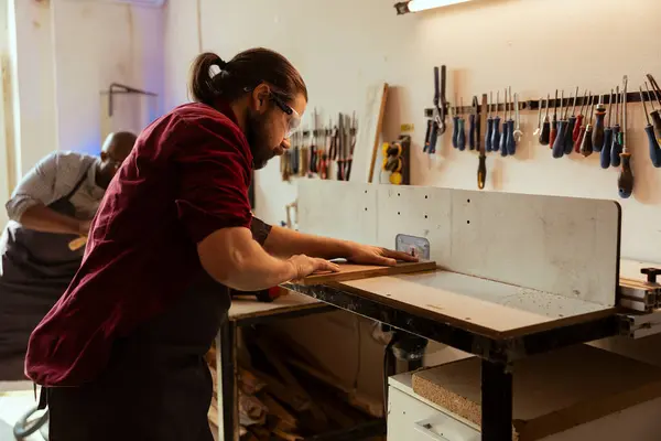 stock image Woodworking expert wears protection gear while inserting plank in spindle moulder to avoid injury. CNC machinist uses safety glasses while cutting lumber with wood shaper to prevent workplace hazards