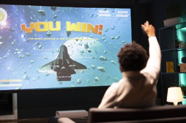 Man playing videogames on gaming console, celebrating victory. Gamer excited after winning online multiplayer game match on widescreen smart TV, rejoicing, throwing fist in air clipart