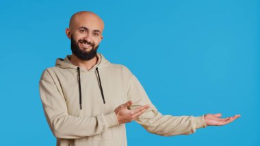 Neşeli adam stüdyo kamerasının önünde reklam yapıyor, mavi arkaplan üzerinde sol ya da sağ tarafı işaret ediyor. Pazarlama kampanyası için reklam ya da reklam gösteren bir ortadoğulu. Kamera 2.