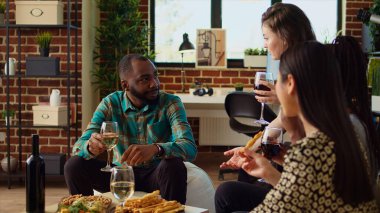 BIPOC 'tan bir grup insan konuşuyor, arkadaşlarıyla buluşurken alkol içiyorlar. Afro-Amerikalı erkek kadınlarla konuşmaktan hoşlanıyor, birlikte eğleniyor, oturma odasında atıştırmalık yiyor.