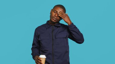 Tired security guard drinking coffee cup to stay awake, being tasked with preventing criminals. Portrait of weary bodyguard sipping caffeinated beverage during night shift, studio background, camera A clipart